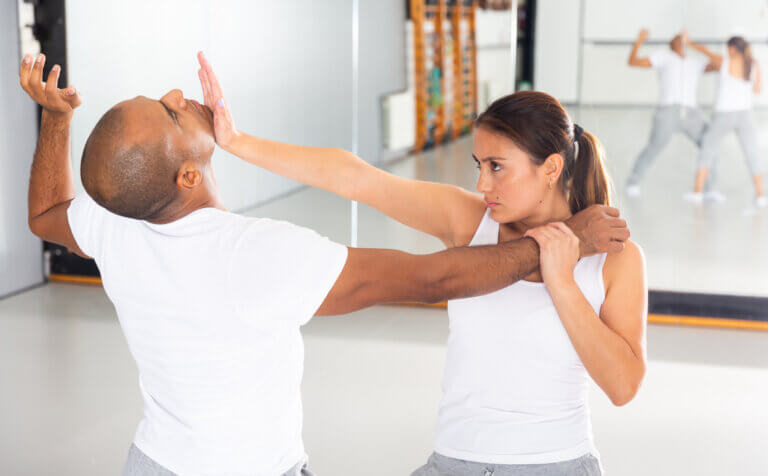 Concentrated Hispanic girl practicing effective self defence techniques with coach in training room, using palm to launch blow in chin
