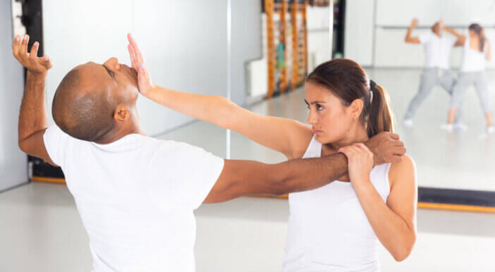 Concentrated Hispanic girl practicing effective self defence techniques with coach in training room, using palm to launch blow in chin