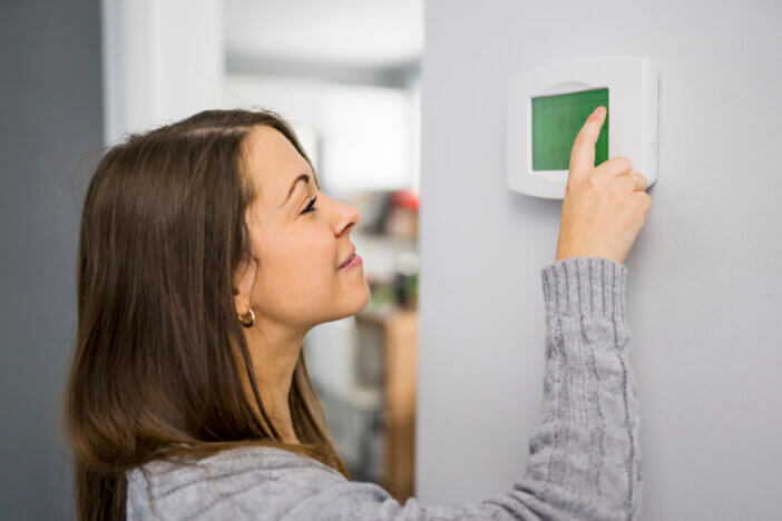A woman set the thermostat at house.