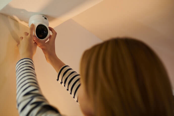 Woman installing security camera on ceiling in apartment