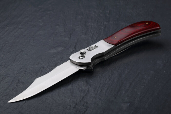 Steel folding knife with an open blade and wooden handle on a stone surface. Steel arms. The concept of weapon, hunting or crime. Material evidence