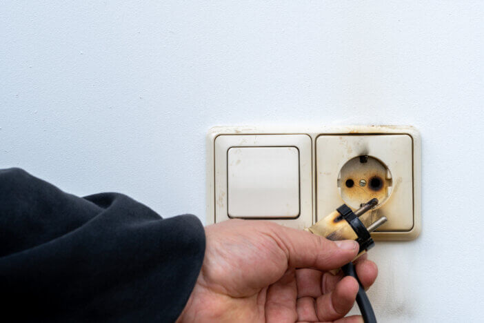 Burned eu style socket in hand. Power Plug after short circuit and fires on white background