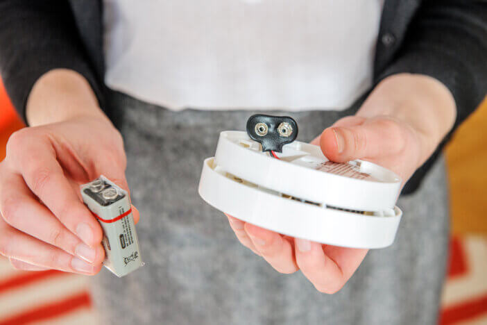 Woman trying to insert a battery in white smoke detector - the device that senses smoke, typically as an indicator of fire