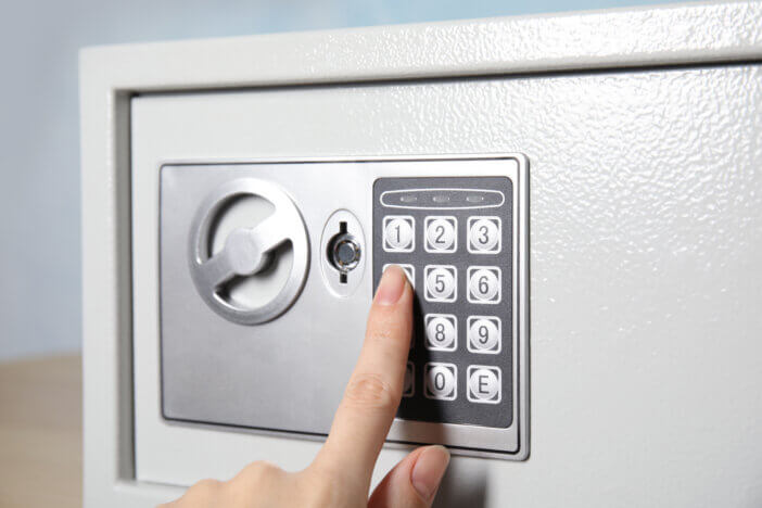 Woman dialing combination on keypad of steel safe, closeup