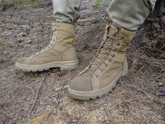 two gray green army high boots made of leather on the feet of a soldier on dry needles and earth in a summer forest
