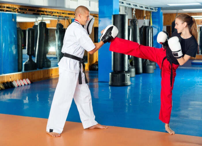 Focused young woman practicing boxing punches in pair with coach during group self defence course in gym