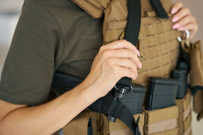 Strong female soldier is wearing a protective body armor, a walkie-talkie, cassettes for a machine gun