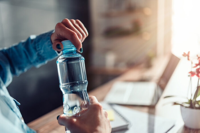 Woman wearing denim shirt working in the office and opening plastic bottle of water