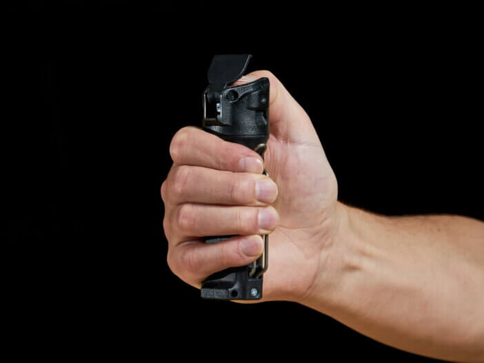male aiming pepper spray on black background