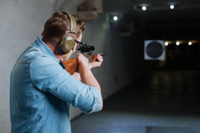 Hitting the bulls eye. Handsome confident serious man holding the rifle and looking into the target while trying to hit the bulls eye