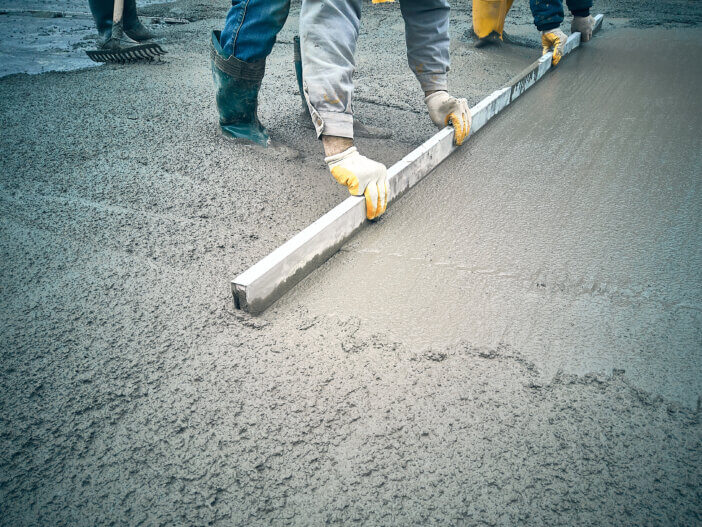 Construction worker uses trowel to level cement mortar screed. Concrete works on construction site. Cast-in-place work using trowels.