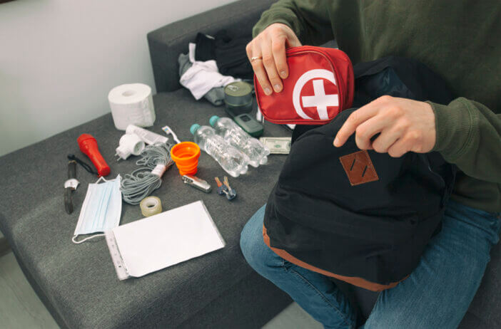 Young man packing the bag with documents, water,food, first aid kit and other items needed to survive