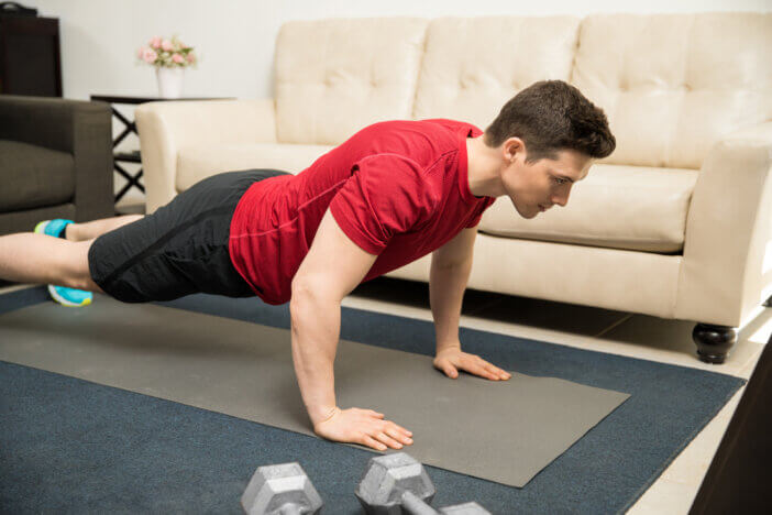 Strong and good looking young man doing push ups on an exercise mat at home