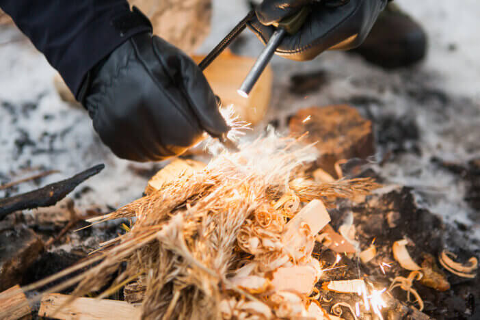 Male hand starts fire with magnesium fire steel, fire striker