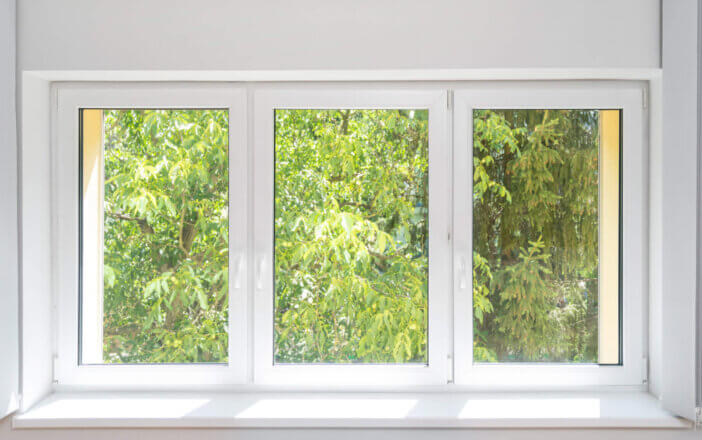 closed plastic pvc window with white frame installed at house, sill and opened vertical fabric jalousie, view on green trees