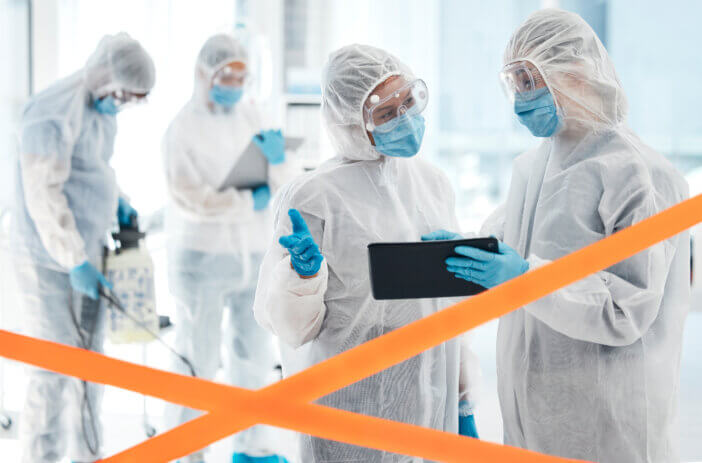 Tablet, covid and team in hazmat suit, cleaning and communicate with face mask for safety from virus. Warning tape, covid 19 and team disinfect hospital for healthcare and bacteria hygiene biohazard