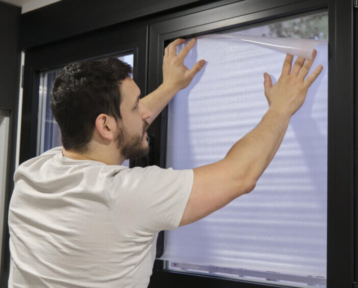 Young latin man installing frosted window vinyl on window glass.