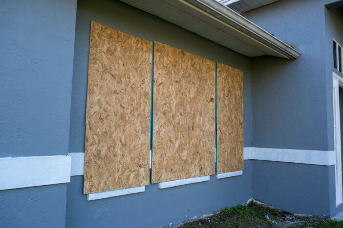 Hurricane shutters made from plywood mounted for protection of house windows. Protective measures before natural disaster in Florida.