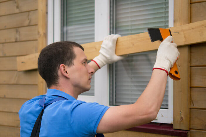 a worker in a blue uniform, boarded up the window of a wooden house, from thieves, when moving to another address, close-up