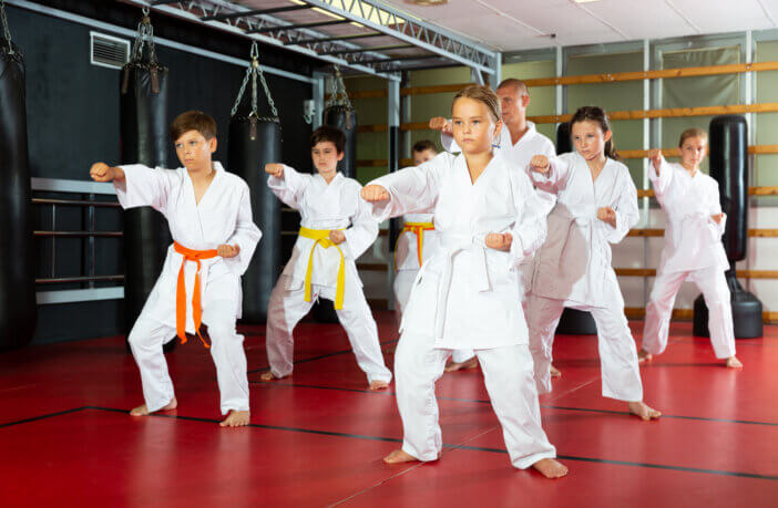Karate kids in kimono performing kata moves with their teacher in gym during group training.