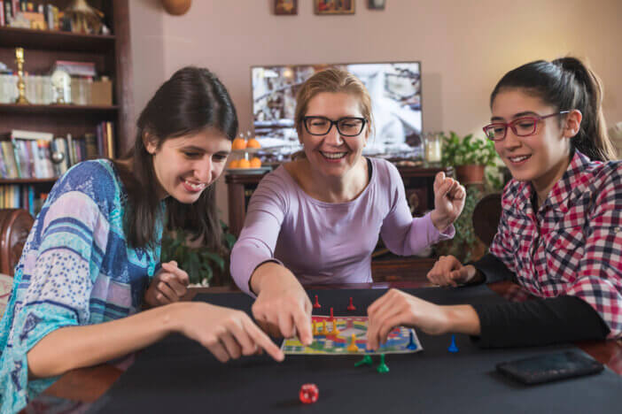 Mother and her teenage daughters playing board games at home