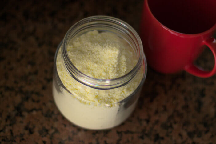 Glass container full of powdered milk along with a red cup. Natural light.