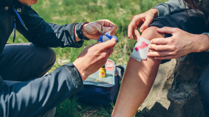 Young man healing knee to a young woman who has been injured doing trekking