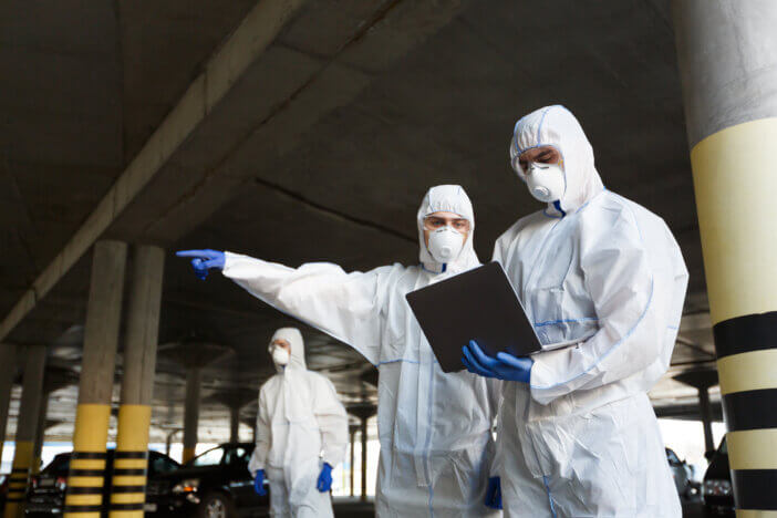 Men in special virus protective suits making research of coronavirus availability on public parking, covid 2019, epidemic