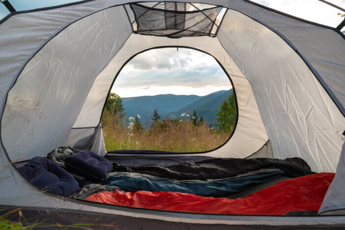 View from the tourist tent on the mountains, meadow, herbs, flowers, early in the morning when the sun rises. Camping equipment including a sleeping bag and pillow. Tourist tent.Turistic background