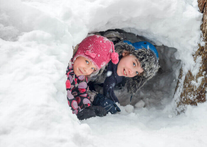 Happy boy and girl looking out from a snow cave they made in a snowdrift
