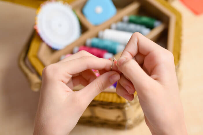 In the hands of a needle, sewing needle and thread on the background of sewing supplies. The thread is inserted into a sewing needle.