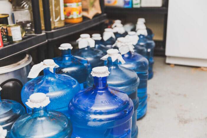 Large blue water bottles in a food storage area. Bottles have temporary fabric lids.