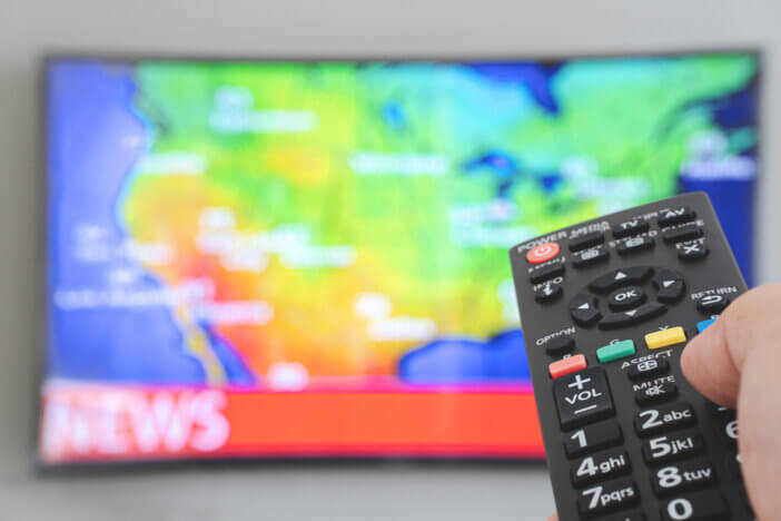 The man switches the news channels on the remote control on TV.