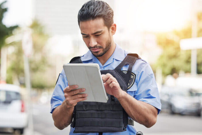 Police, tablet and patrol with a man officer outdoor on the street, using the internet to search during an investigation. Technology, information or law enforcement with a male security guard on duty