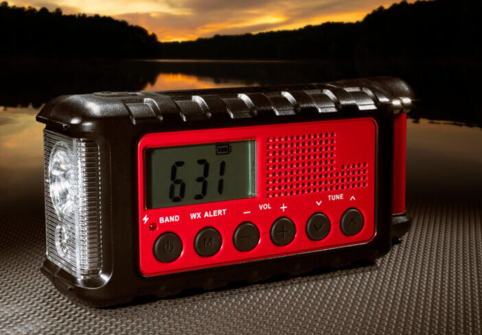 Sun glowing on the horizon over a lake's water with a red weather radio in the foreground.