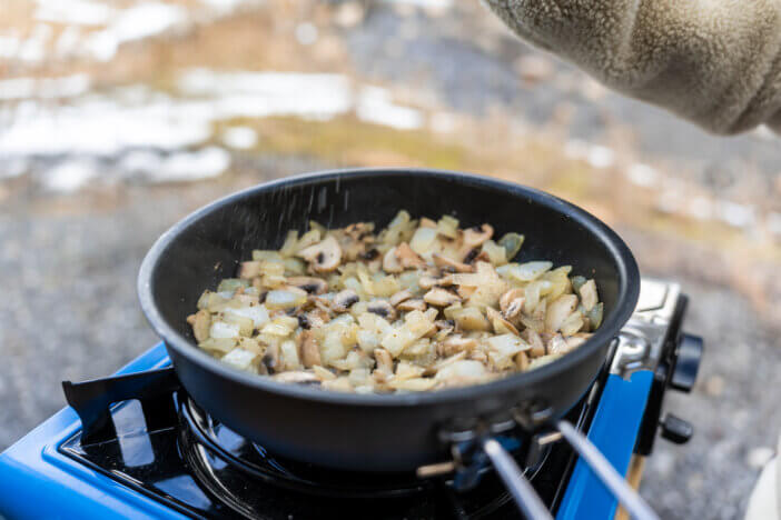 A camping pan frying onions and mushrooms, outdoors in a van, during the winter season.