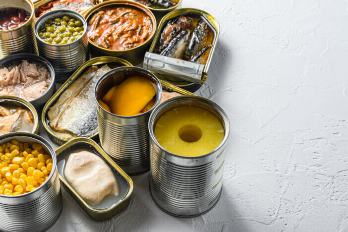 Tin cans for processed food cans conserve Saury, mackerel, sprats, sardines, pilchard, squid, tuna pinapple, corn, peas, mango , beans, over white textured background close up side view space for text.