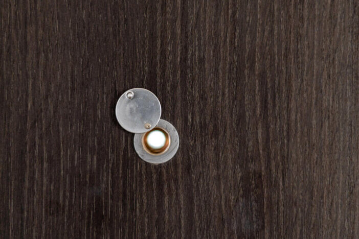 Close up view of home peephole with metal lid cover on a brown wooden door with copy space. Reliable protection in a house. Privacy and safety concept