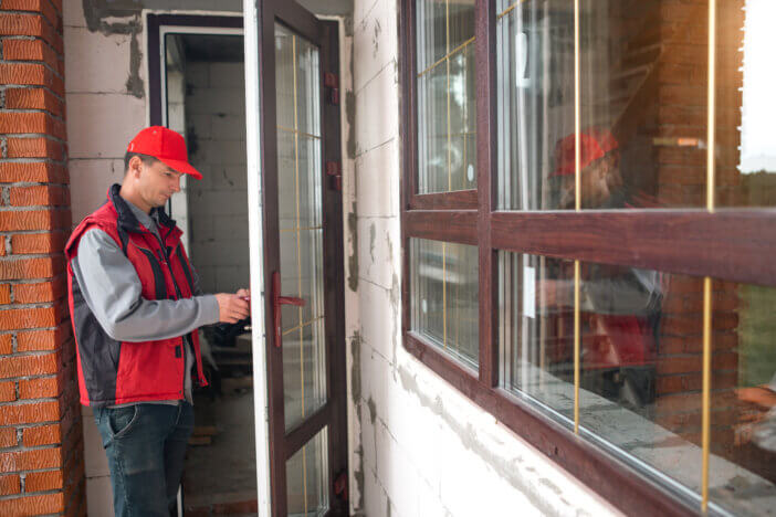 Master sets up a door handle with multi-lock plastic door with wood lamination and gold layout in private house. Installation of windows and doors, glazing of the cottage, replacement of the mechanism