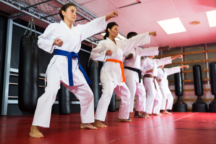 Polyethnic men and women wearing kimono and belts. Group of people doing kata during karate training.