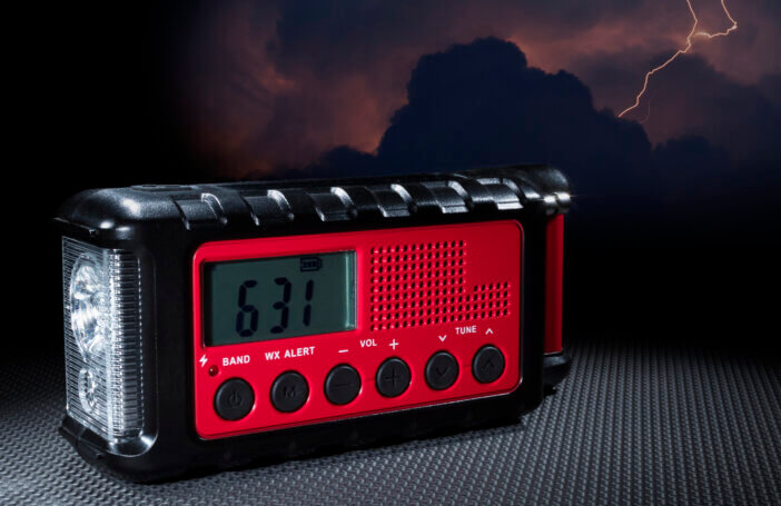 Electric storm behind a red weather radio that has a flashlight and clock built in.