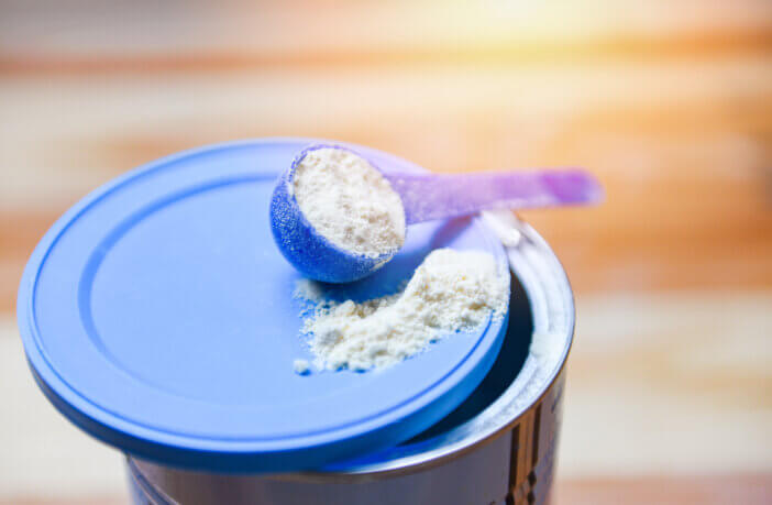 Milk powder in spoon on can for baby and wooden table background