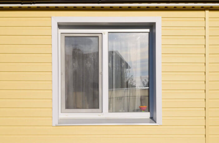 The wall of a private house with a window covered with yellow siding