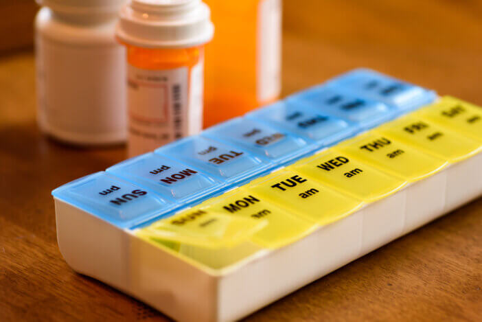 Using a pill holder to keep track of medication doses, pill organizer and prescription bottles on table
