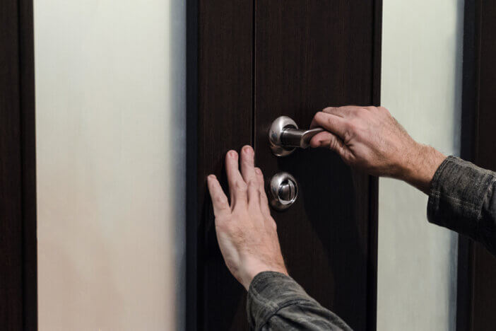 Hands closing the double door. A man carpenter checks the door sheet closing and a handle with a lock during installation.