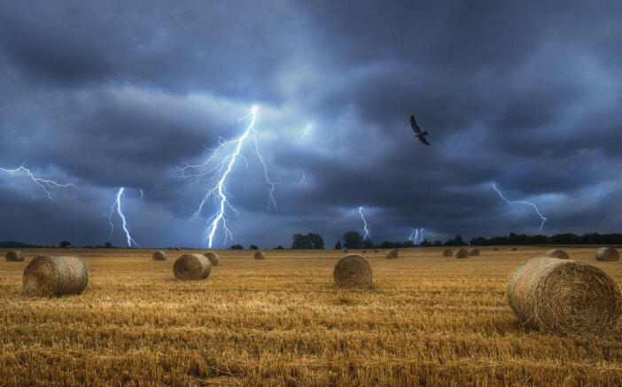 Bales of hay on the field during a lightning storm. Force of nature landscape. Agricultural field with straw bales and lightning bolts. Countrylife.