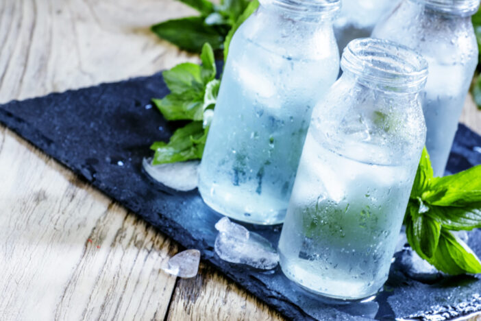 Very cold mineral water with ice in a misted glass bottles, dark background, selective focus
